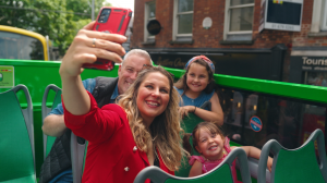 family of four taking a selfie on the tour bus  woman taking a picture of her family on top of the hop on hop off tour bus